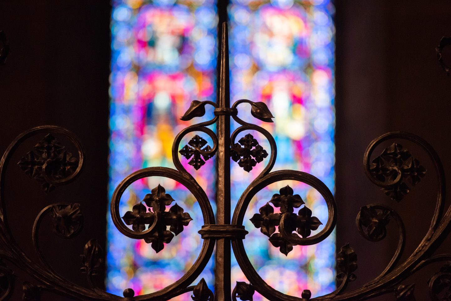 Detail of ironwork against backdrop of colorful stained glass window