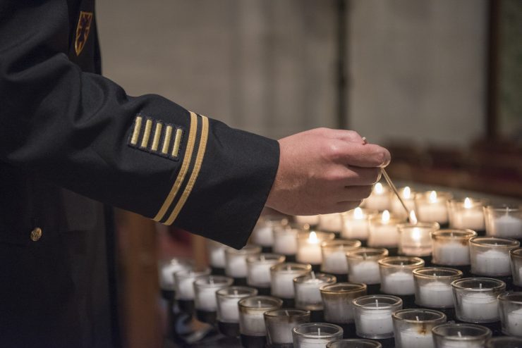 Close-up of someone in military uniform lighting a votive candle in prayer