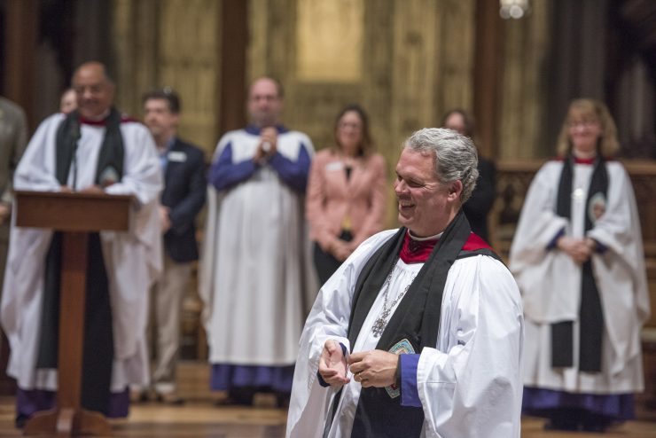 Dean Hollerith smiling, during a service, with other Cathedral Clergy and staff in the background