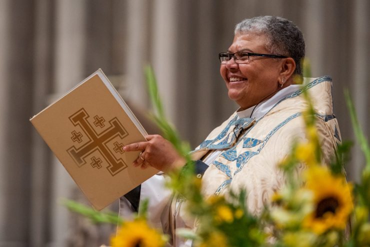Smiling clergy holding service book with sunflowers in the foreground