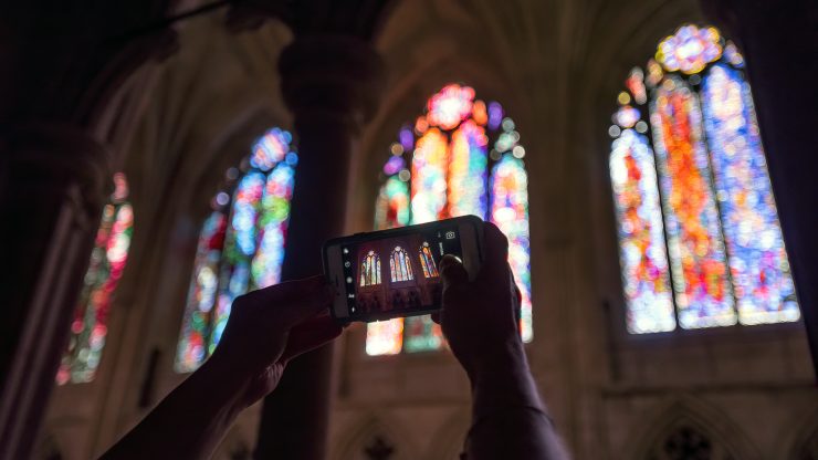 Close-up of visitor taking photo of stained glass windows during sightseeing tour