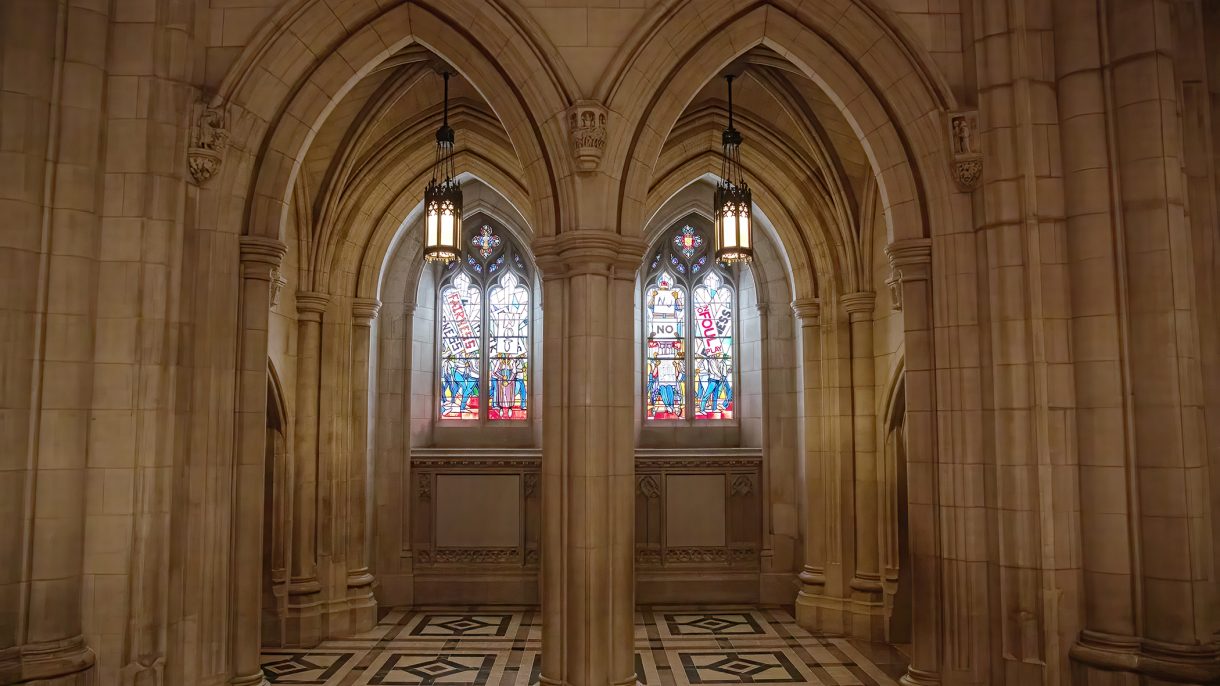 Frontal view of four lancets of stained-glass windows in a neo-Gothic Cathedral bay with light filtering through