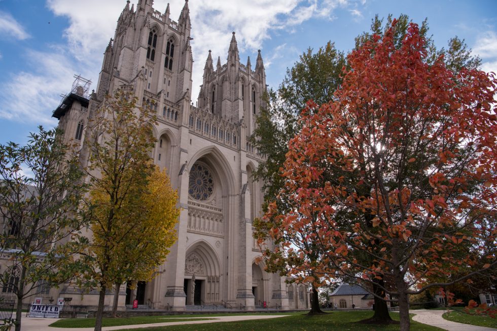 Front view of two Cathedral towers behind trees with yellow, red, and green leaves.