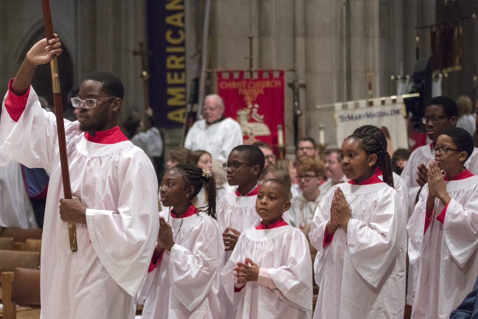 A young adult acolyte leads a group of youth acolytes down the aisle.