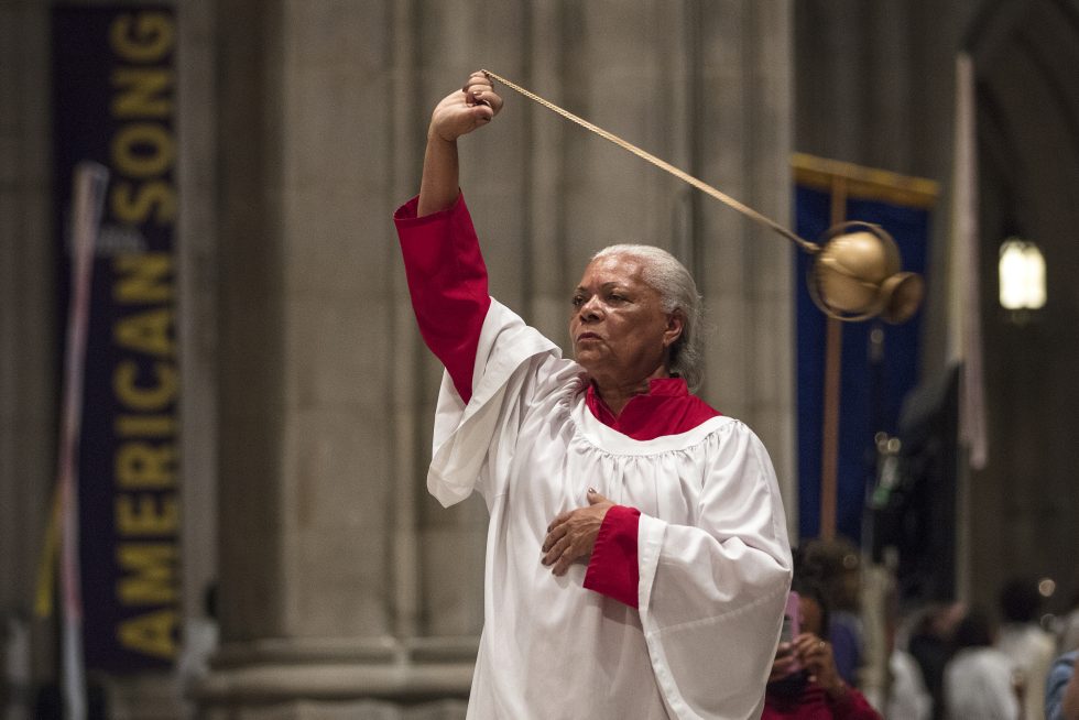 An older adult acolyte swings a thurible over their head.