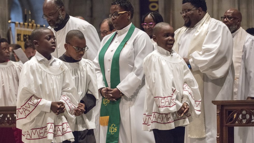 Children and adults in acolyte vestments walk down the Cathedral aisle.