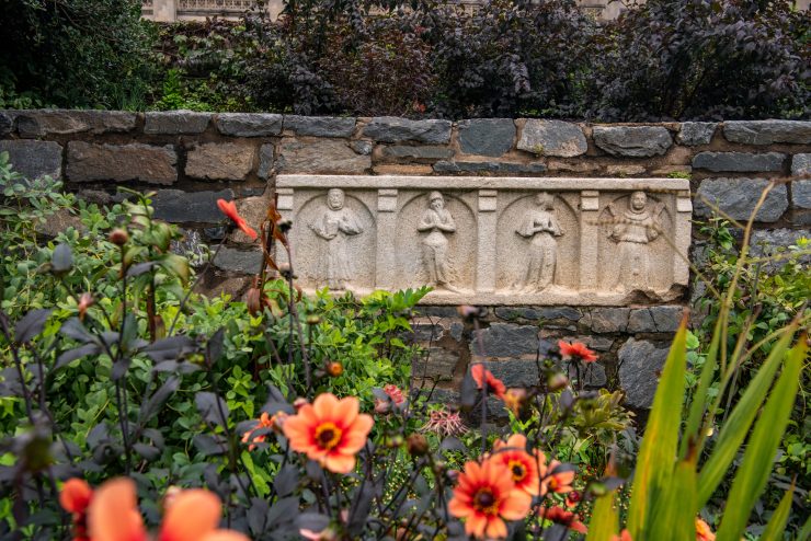 Orange flowers and green foliage against a stone wall with limestone carving.