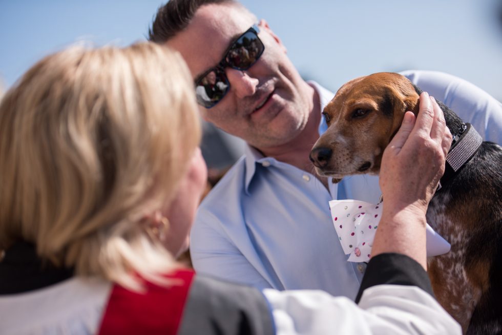 A clergy person greets a small dog wearing a bow tie.