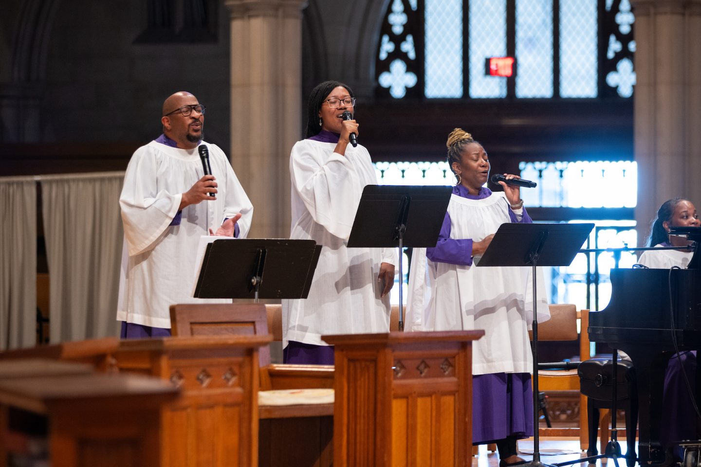 Singers in white choir robes perform in front of gothic architecture.