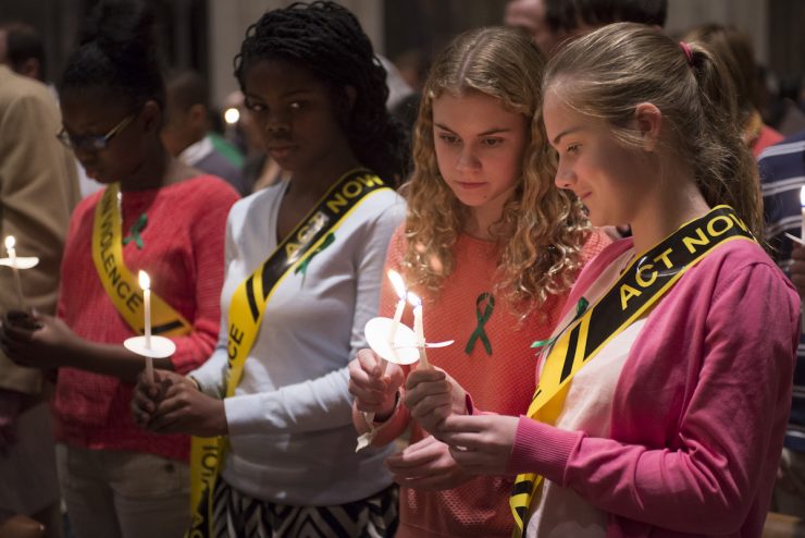 Girls lighting candles, wearing sashes reading, "act now"