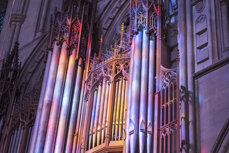 Cathedral's organ with colorful light projected on it from the stained-glass windows